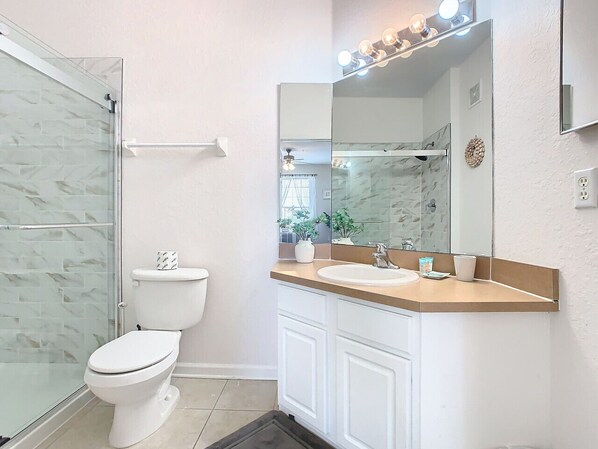 A bathroom with a glass shower enclosure, a toilet, a sink with a mirror, and a towel rack.