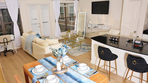 Una sala de estar moderna con un sofá, una mesa de comedor para cuatro personas y una zona de cocina con barra.