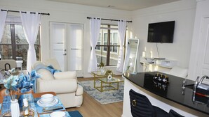 Una sala de estar moderna con un sofá, una mesa de comedor con platos y cubiertos, una mesa de centro y un televisor montado en la pared.