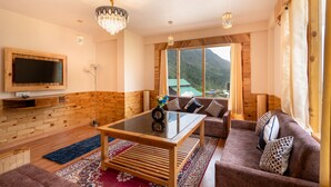 A cozy living room with a wooden floor, a glass coffee table, a brown sofa, and a large window offering a mountain view. - Chirag Haveli Retreat (Manali)
