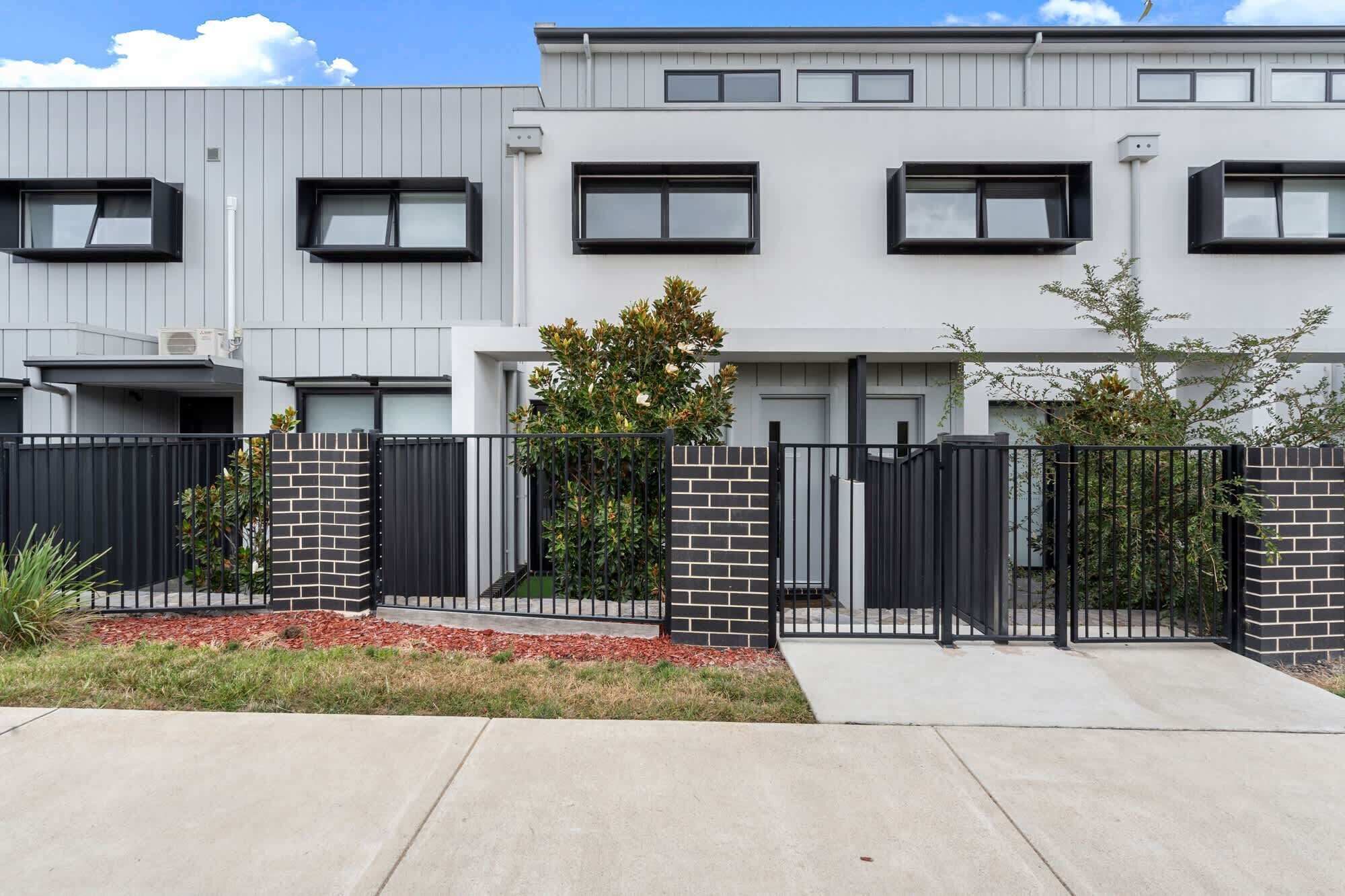 A modern residential building with a grey facade, multiple windows, and a gated entrance.