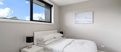 Un dormitorio con cama, mesita de noche, lámpara y ventana con vista al cielo.