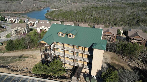 A multi-story building with a green roof, balconies, and a view of a lake and forested hills. - 51-06 Eagles Ridge Retreat, Spacious walk-in.  Balcony, mountain views, indoor/outdoor pools/splash pads.  Close to SDC. (Branson)