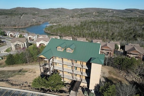 A multi-story building with a green roof, balconies, and a view of a lake and forested hills.