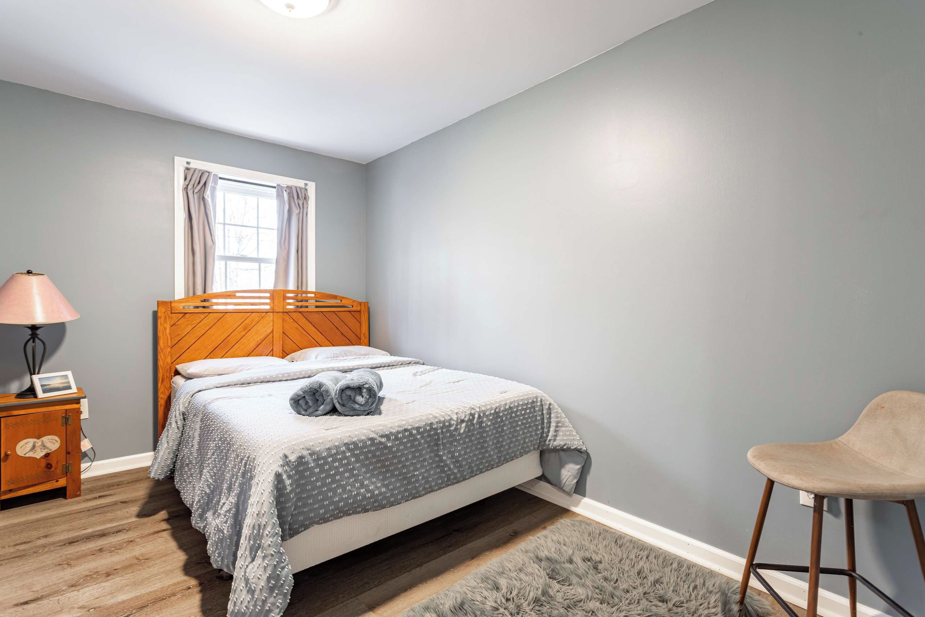 A bedroom with a wooden bed, a nightstand with a lamp, a chair, and a window with curtains.