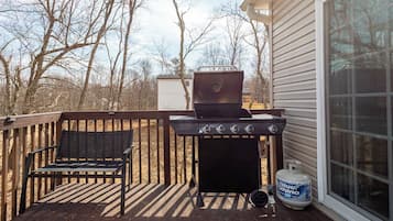 Una terraza con una parrilla, un cilindro de gas y un banco.