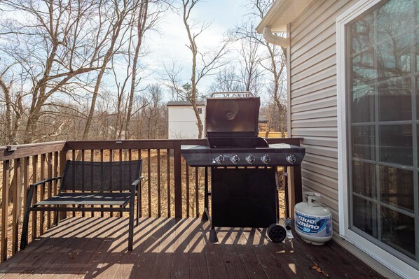 A deck with a grill, a gas cylinder, and a bench.