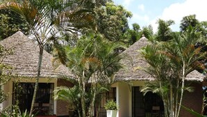 Un bungalow au toit de chaume, entouré d’une végétation luxuriante et de palmiers.