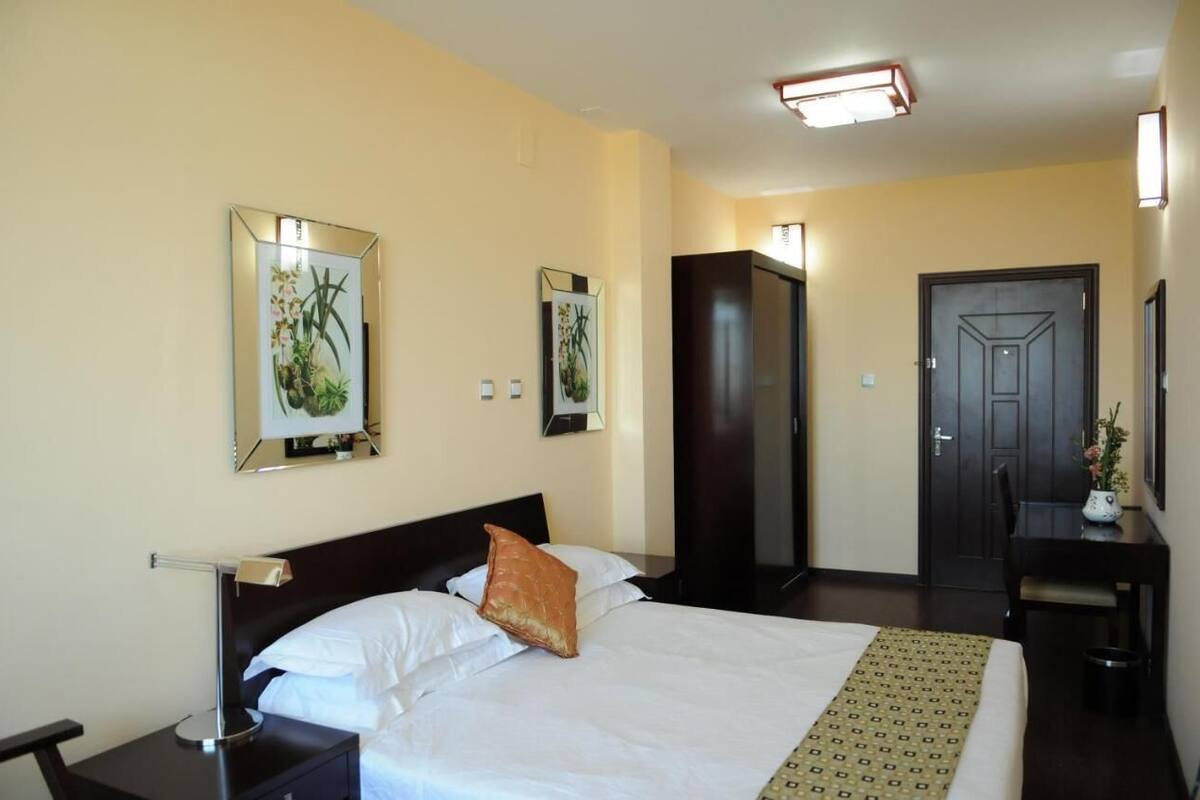 A hotel room with a bed, bedside table, lamp, and two framed pictures on the wall.