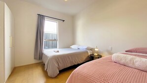 A bedroom with a bed, a bedside table with a lamp, a window with curtains, and a wooden floor. - 6mins to airport. Large Family House. (Auckland)