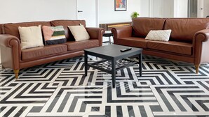 A modern living room with two brown leather sofas, a black coffee table, and a geometric patterned floor. - 6mins to airport. Large Family House. (Auckland)
