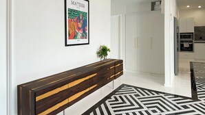 A modern hallway with a wooden console table, a framed artwork, and a geometric patterned rug. - 6mins to airport. Large Family House. (Auckland)