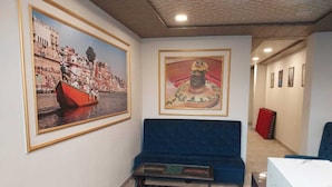 A hotel lobby with a blue sofa, a marble reception desk, and two framed artworks on the walls. - Kashi Kutir (Varanasi)