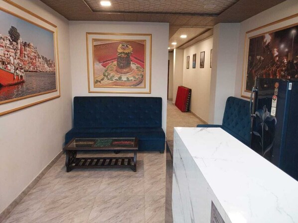 A hotel lobby with a reception desk, a blue sofa, a small table, and framed artwork on the walls. - Kashi Kutir (Varanasi)
