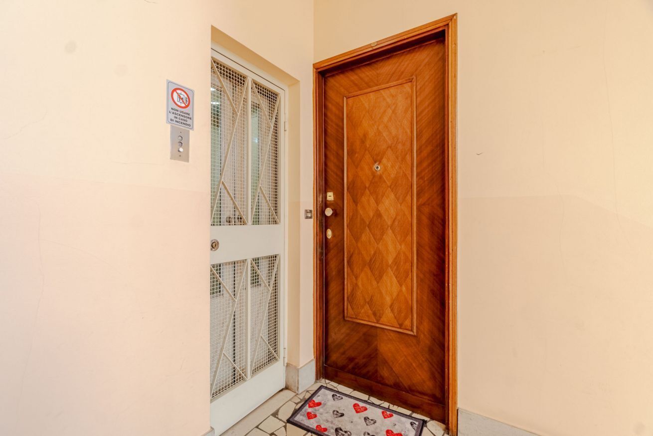 A wooden door with a diamond-patterned panel, a metal mesh window, and a doormat with heart designs.