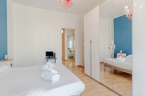 A hotel room with a large bed, a bedside table with a TV, a mirror, and a wardrobe. - GuestHost - Cozy&Bright Apartment X2 MM1 Paradiso (Torino)