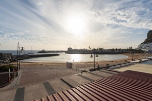 A coastal promenade with a beach, a rocky outcrop, and a pier. - Apartment in Mogan by Mogan Beach (Mogan)