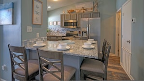 A modern kitchen with granite countertops, stainless steel appliances, and a dining area with four chairs. - Stylish 2BR Coastal Getaway w/ Pool & Prime Location | Lazy Fun (Port Aransas)