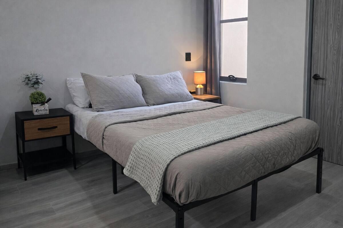A bedroom with a bed, bedside table, lamp, and a window.