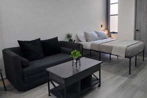 Uma sala de estar moderna com um sofá cinza escuro, uma mesa de centro harmoniosa e uma cama com colcha cinza.