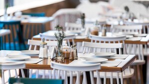 A restaurant with round tables set for dining, white chairs, and a central decorative arrangement of a glass jar, salt shaker, and a sprig of rosemary. - Cavo Grosso Bungallows (Mavrovouni)