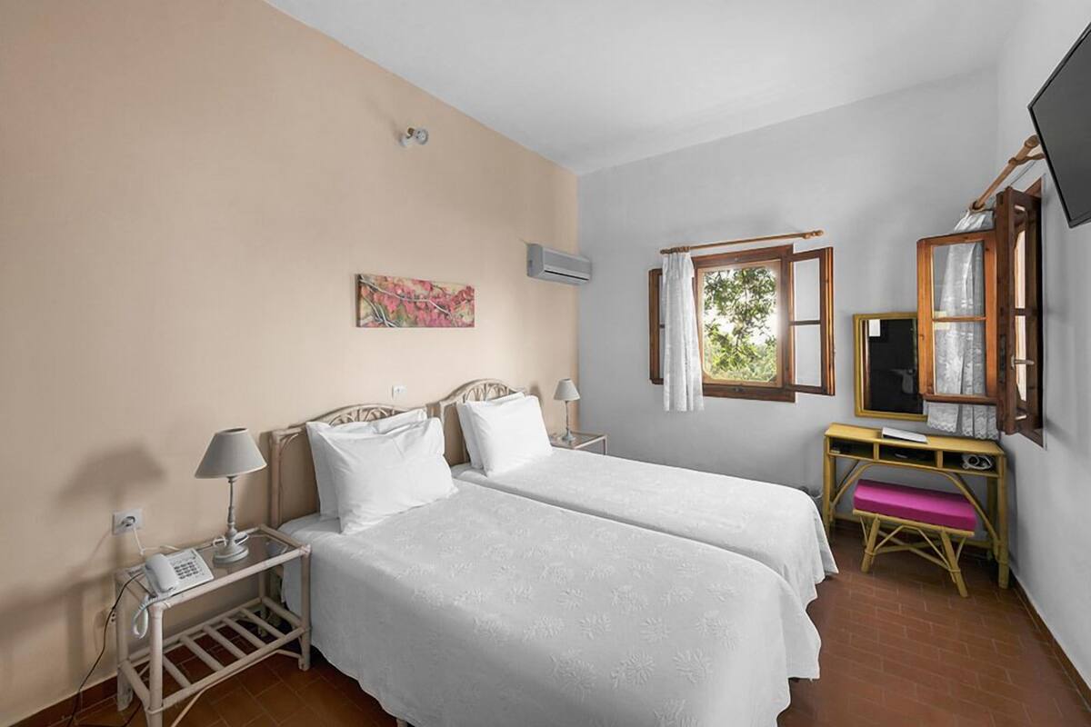 Une chambre avec deux lits, un bureau, une chaise, une télévision et une fenêtre avec des rideaux.