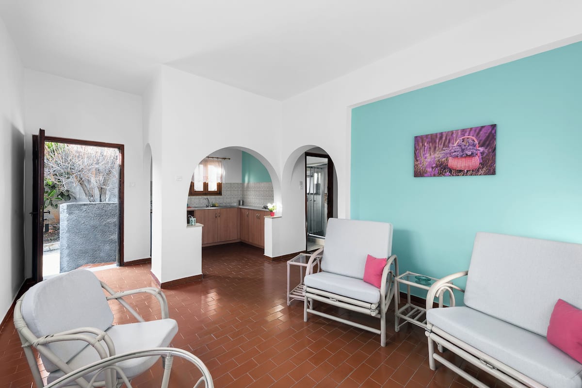 Un vaste espace de vie avec des meubles blancs, une cuisine à l’arrière-plan et un mur d’accent de couleur turquoise.