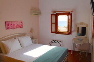 A bedroom with a bed, a desk, a chair, a window with a view, and a wall-mounted air conditioner.