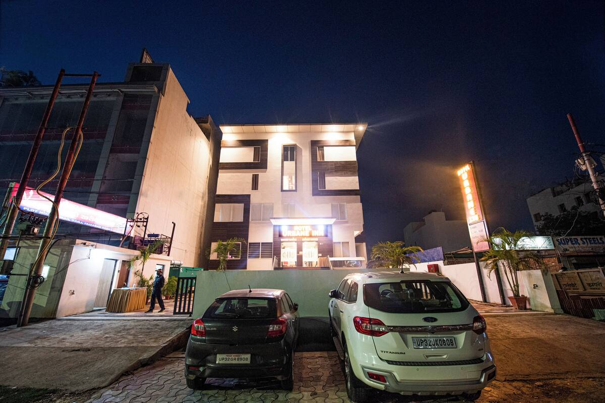 A hotel with a modern facade, a well-lit entrance, and two parked cars in front.