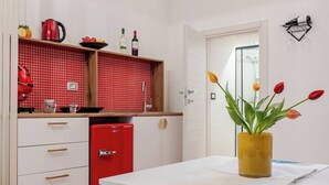 A modern kitchen with white cabinets, a red refrigerator, and a red backsplash. There is a dining table with a yellow vase of tulips.