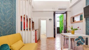 A modern living room with a yellow sofa, a dining area with a white table, and a kitchen with red cabinets.