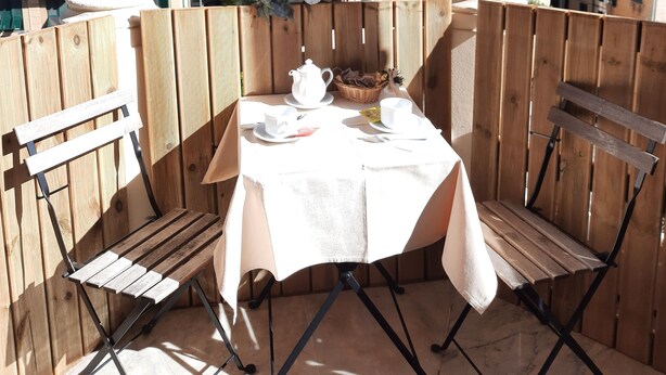 A balcony with a table set for two, overlooking a cityscape with historic buildings. - Rooms Palazzo Groppallo  (Genoa)