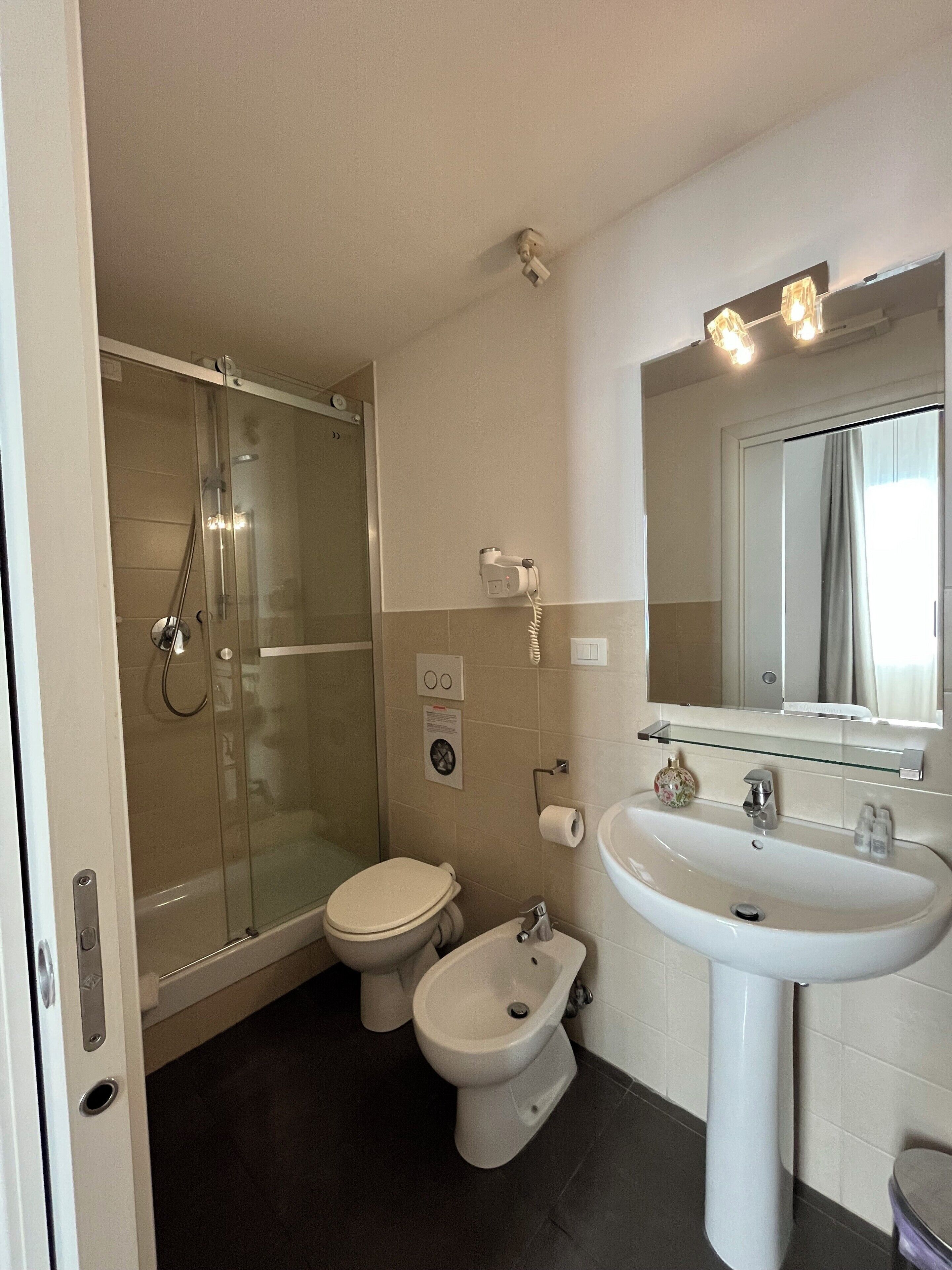 Eenvoudige driepersoonskamer | Badkamer | Een douche, een haardroger, handdoeken, zeep
