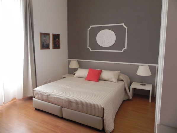 A bedroom with a bed, two bedside tables, a wall-mounted lamp, and a framed picture. - Rooms Palazzo Groppallo (Genoa)