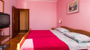 A room with pink walls, a bed with a red blanket, a television on a wooden stand, and a painting on the wall. - Apartments Neve - One-Bedroom Apartment with Balcony and Sea View (Zaton)