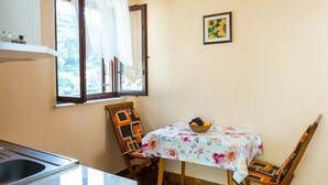 A small dining area with a table set for two, a window with curtains, and a framed picture on the wall. - Apartments Neve - One-Bedroom Apartment with Balcony and Sea View (Zaton)