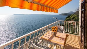 Un balcón con una mesa y sillas, un jarrón con girasoles y vistas al mar y montañas a lo lejos.