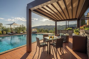 Zona piscina con un pergolato, posti a sedere all'aperto e vista sulle montagne.