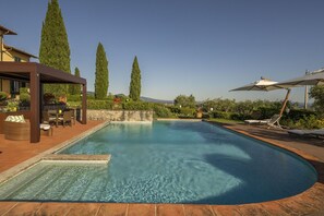 A swimming pool with a pergola, lounge chairs, and a view of the landscape.