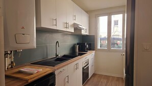 A compact kitchen with a sink, stove, and microwave. There is a window providing natural light and a view of the outside.