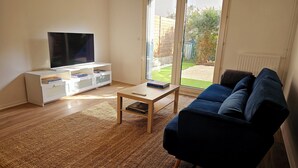 A living room with a TV on a white entertainment unit, a blue sofa, and a small wooden coffee table.