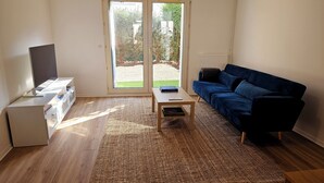A living room with a sofa, a coffee table, a TV, and a sliding glass door leading to a garden.