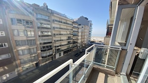 Een hoog gebouw met meerdere balkons, een helder uitzicht op de straat en een strand in de verte.