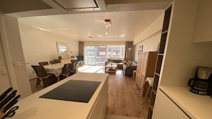 Een moderne keuken met een centraal eiland, een eethoek met stoelen en een zithoek met een bank en een koffieapparaat.