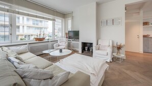 A modern living room with a sofa set, a fireplace, a TV, and a view of the outside balcony.