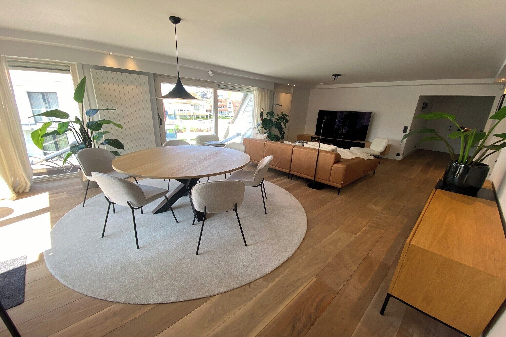Een moderne woonkamer met een ronde eettafel, banken en een televisie.