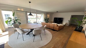 A modern living room with a round dining table, sofas, and a TV. - Duplex in Knokke-Heist near Beach & Casino (KNOKKE-HEIST)