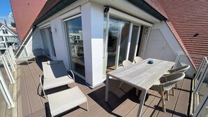 A covered outdoor deck with a table and chairs, a sliding glass door, and a view of neighboring buildings. - Duplex in Knokke-Heist near Beach & Casino (KNOKKE-HEIST)