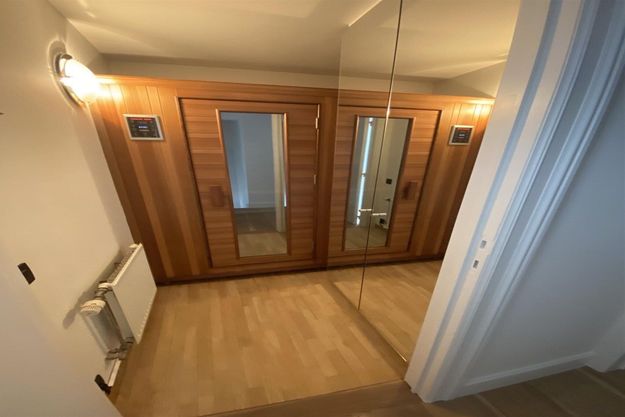 Een gang met houten lambrisering, een radiator en een spiegel aan de muur.