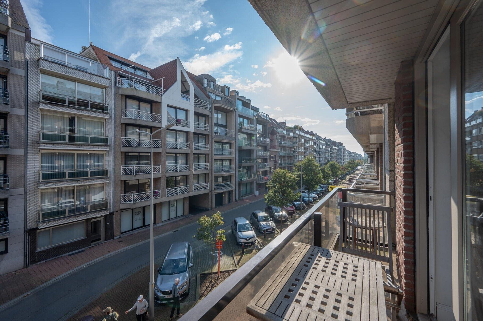 Un immeuble d’habitation doté de nombreux balcons, donnant sur la rue, avec des voitures garées devant.